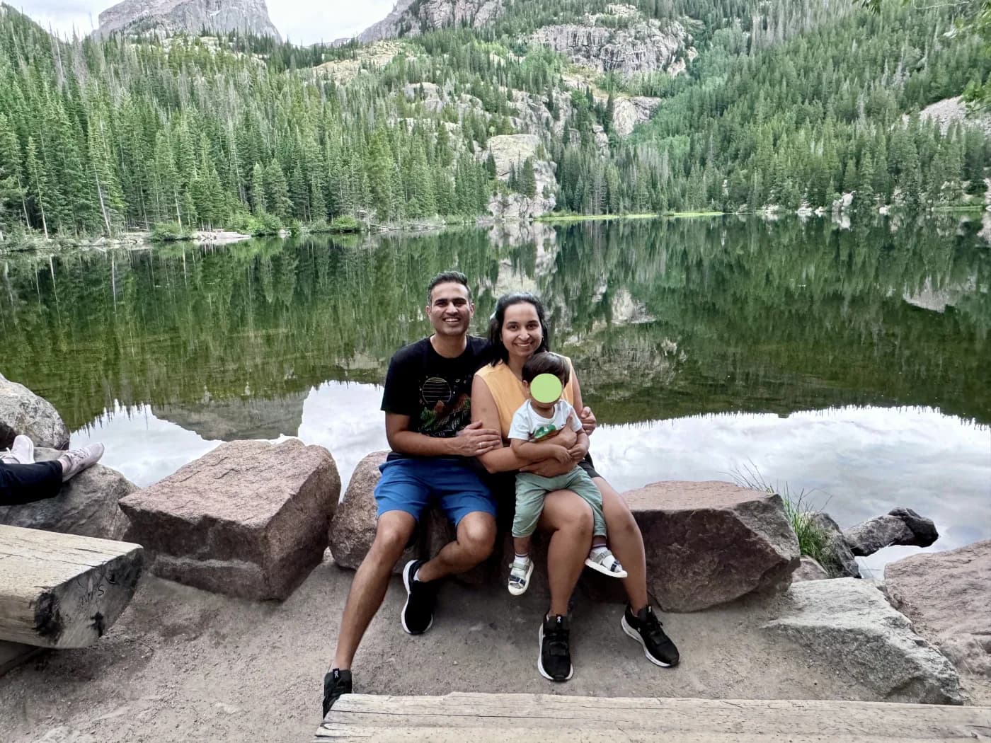 Karan and Priyanka with their son on a family hike by a mountain lake